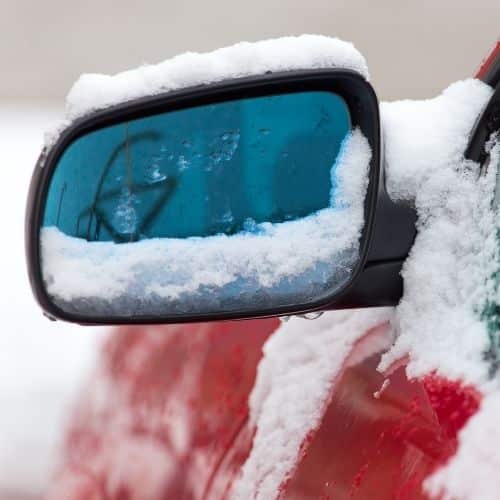 Side mirror on car covered in snow.