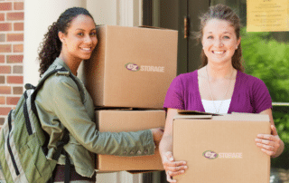 Two women standing outside a college dorm holding moving boxes.