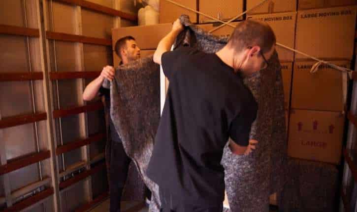 Two men covering furniture in storage.