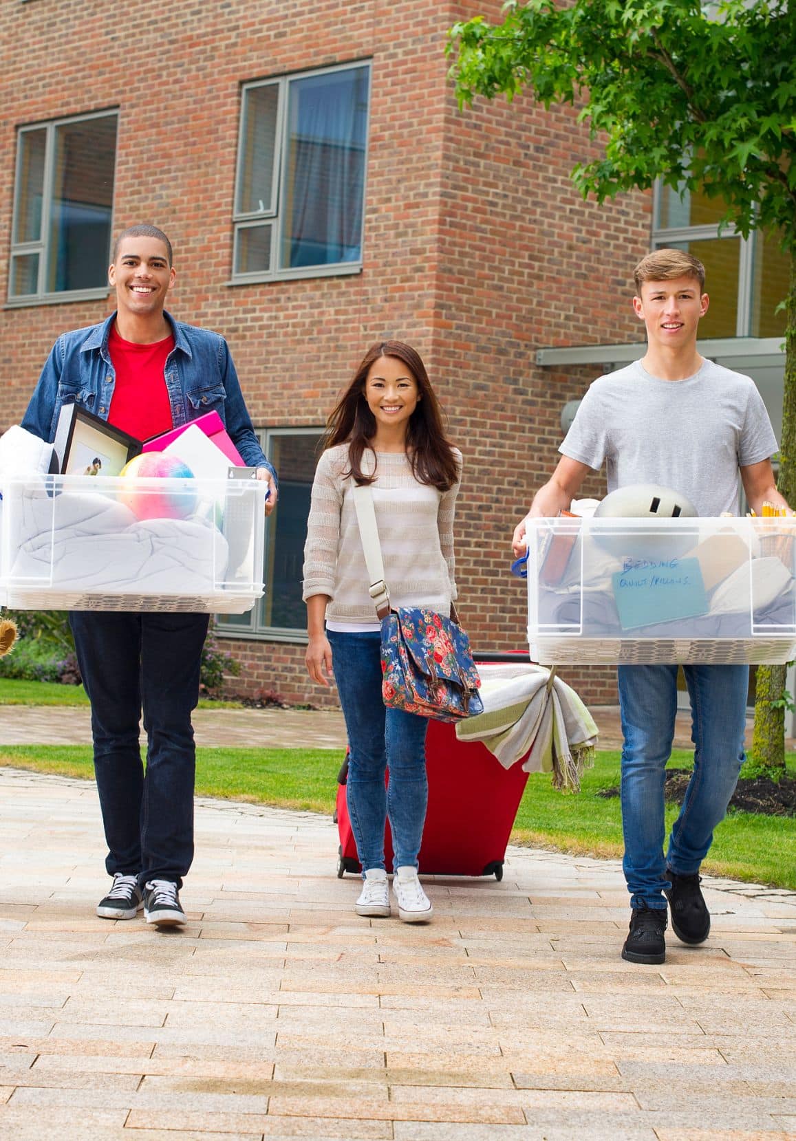 group of three students on campus carrying luggage and storage bins