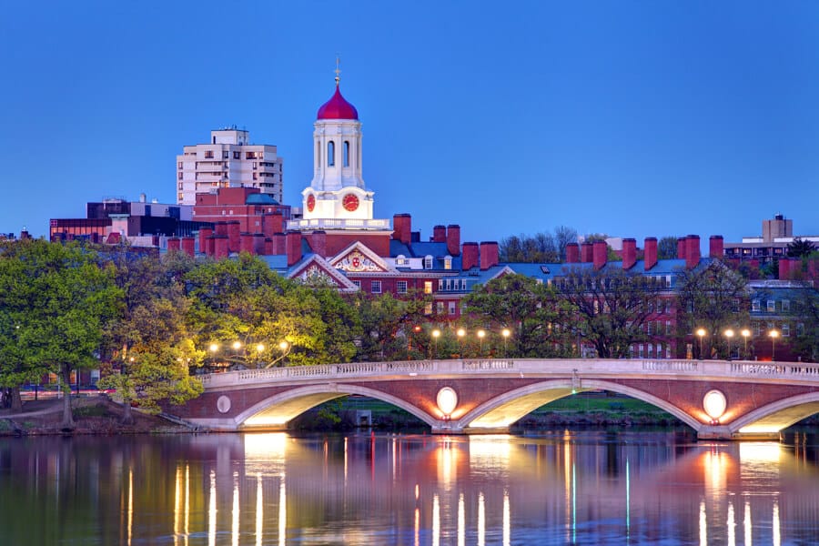 view of a bridge over water with harvard college building in the background at dusk.