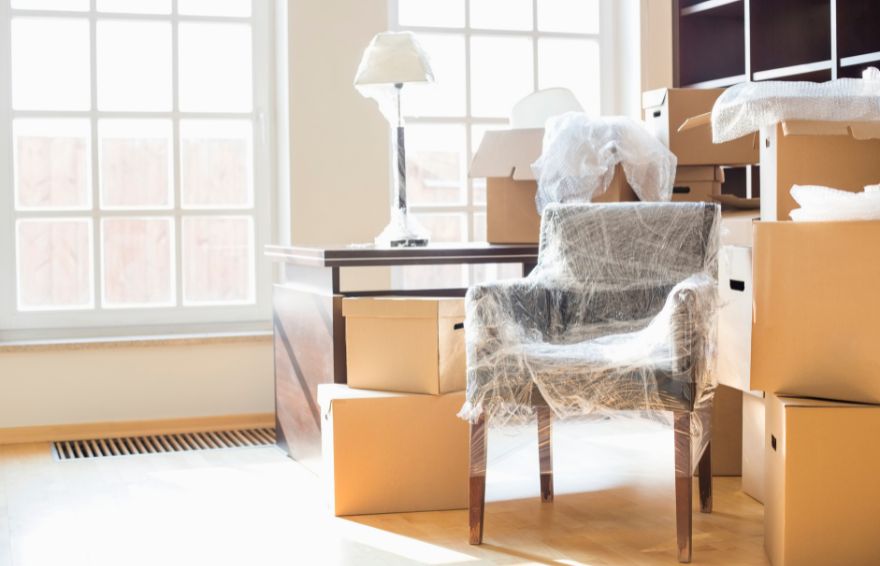 Furniture wrapped in plastic next to cardboard boxes in an empty room.