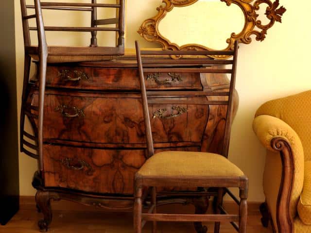 Group of antique wood furniture stacked in a room.