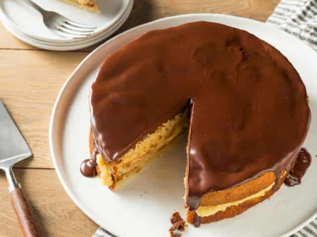Photo of a Boston cream pie sitting on a plate with one piece missing.