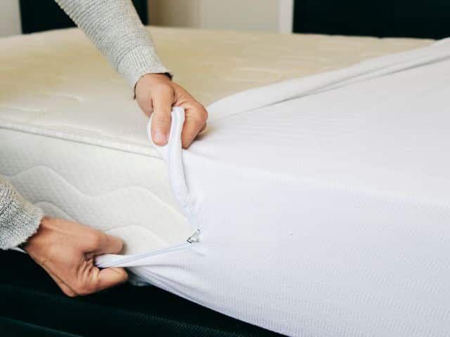 Person pulling a cover onto a bed mattress for storage.