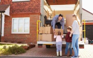man, woman and child putting cardboard boxes into the back of a moving truck at their home