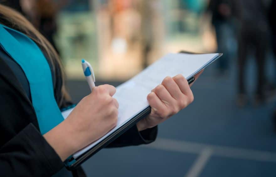 up close perspective of a hand using a pen to write on a paper on a clipboard