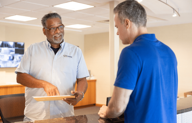 two men talking at a counter with one man pointing at a clipboard