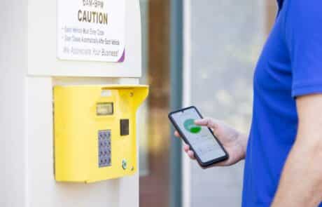 person holding a mobile phone next to a bright yellow entry keypad