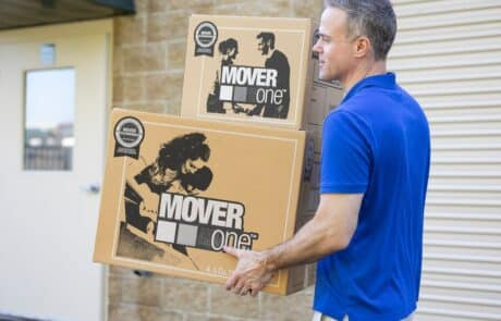 man in blue shirt walking with two moving boxes in his hands