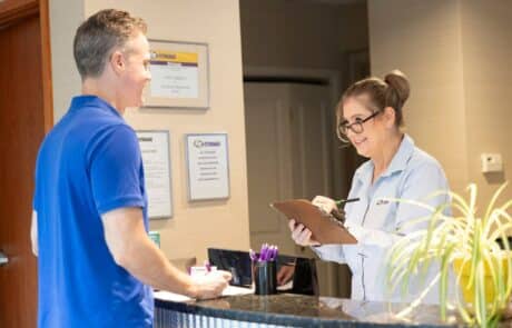 woman behind a counter writing down information on a clipboard while a man talks with her