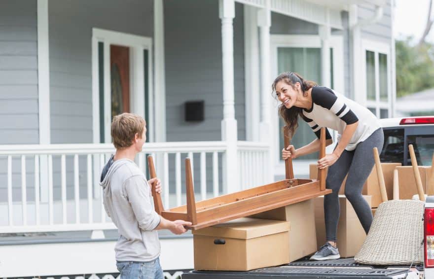 man and woman moving furniture together from the back of a truck into a home